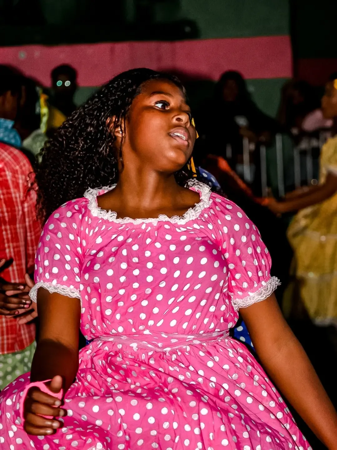 Mulher de vestido rosa com bolinhas brancas olhando para o lado em uma festa.