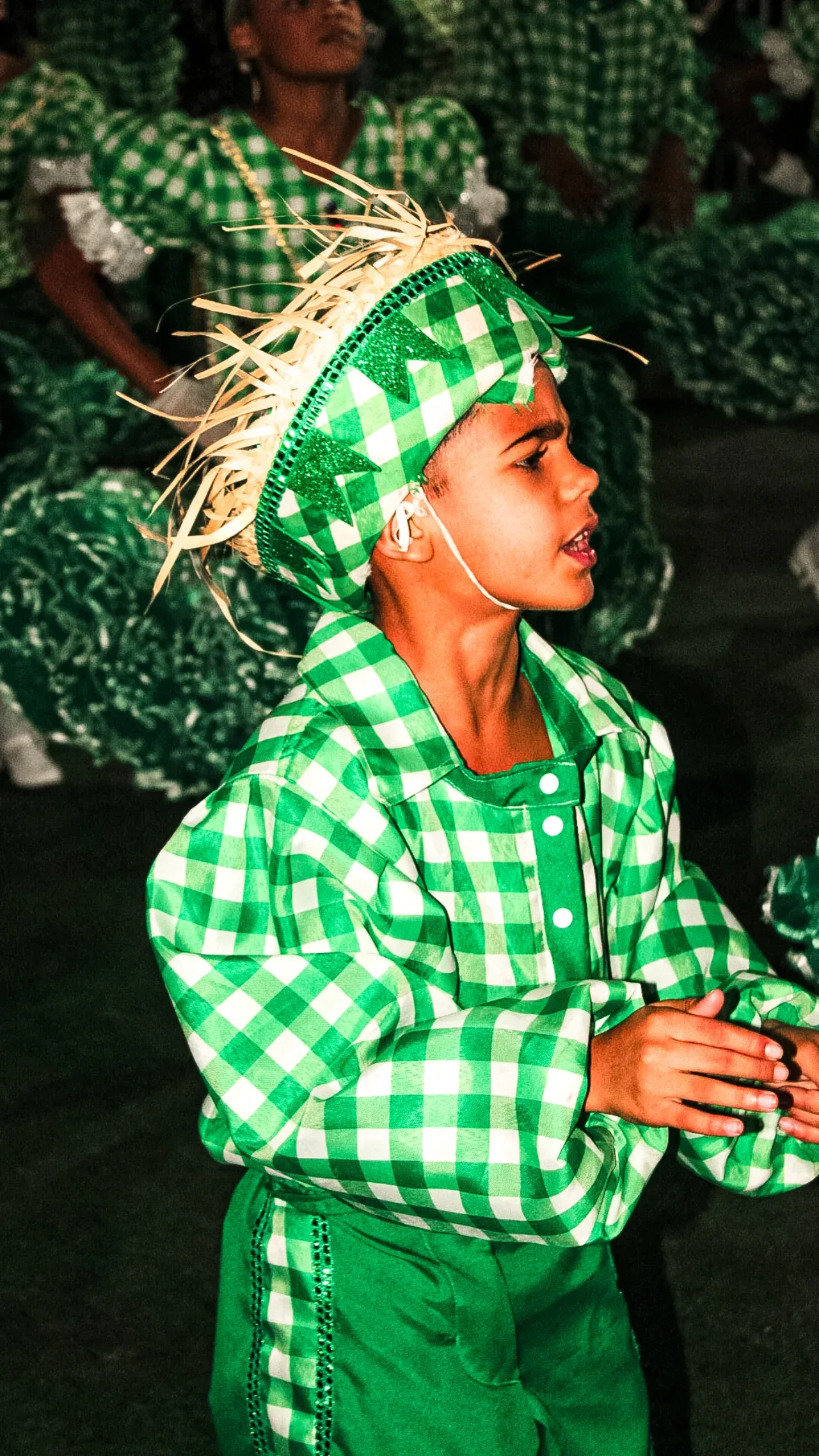 Jovem de roupa xadrez verde e chapéu decorado em uma festa junina.