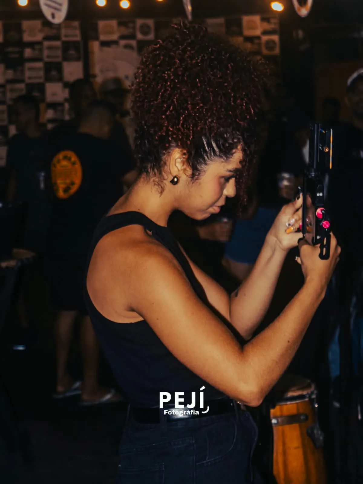 Mulher de roupa preta fotografando com o celular em um ambiente com luz baixa.