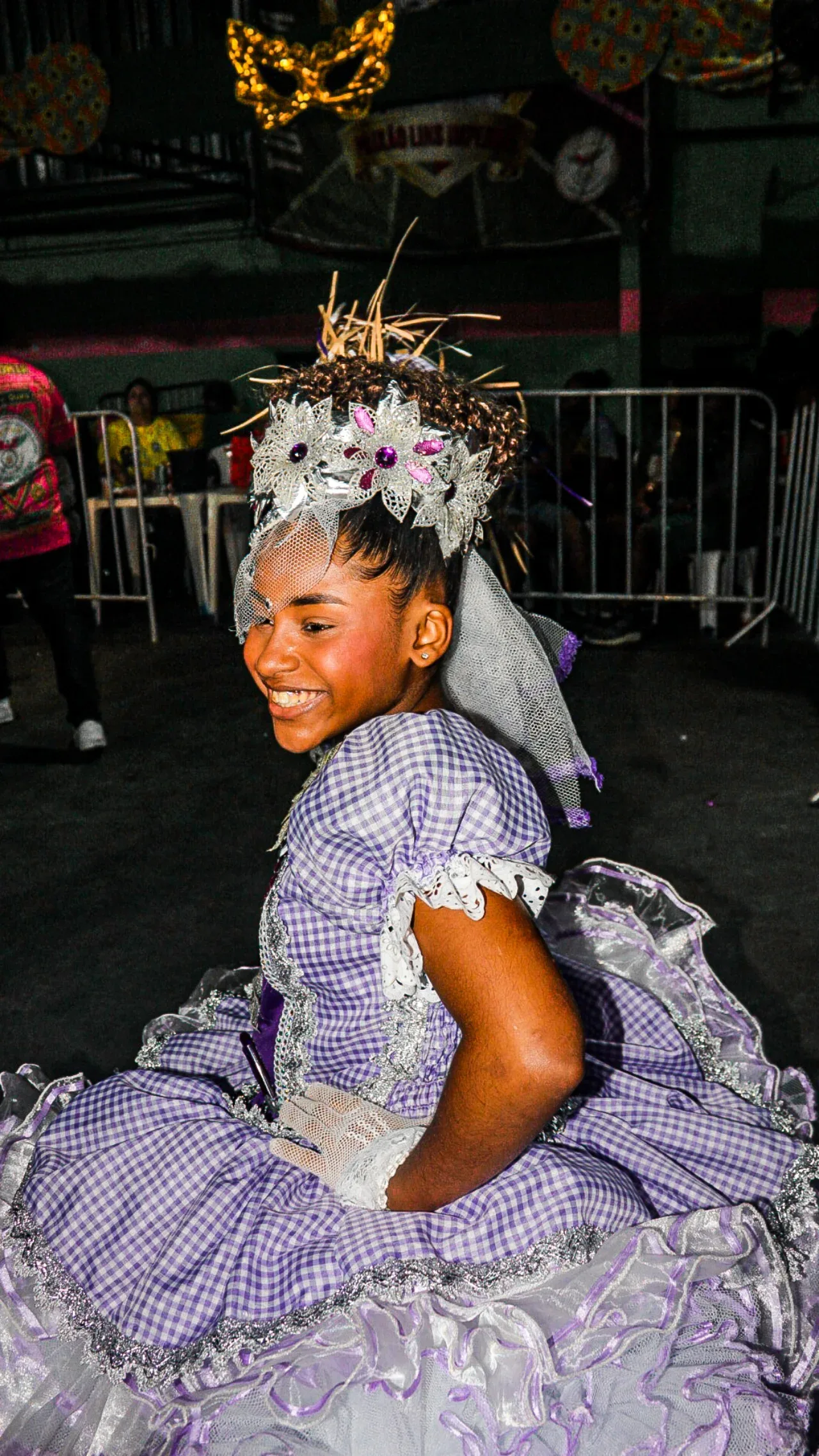 Dançarina com vestido lilás e adereço de flores no cabelo em uma apresentação.