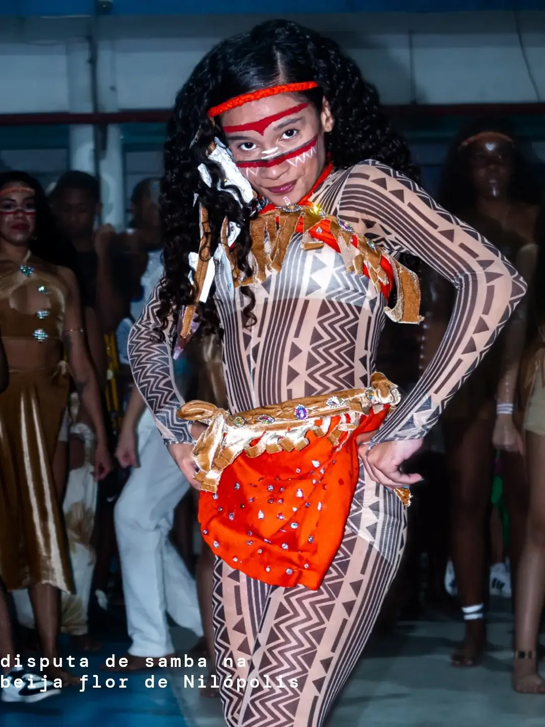 Dançarina de samba com fantasia estampada, adereços vermelhos e laranja.