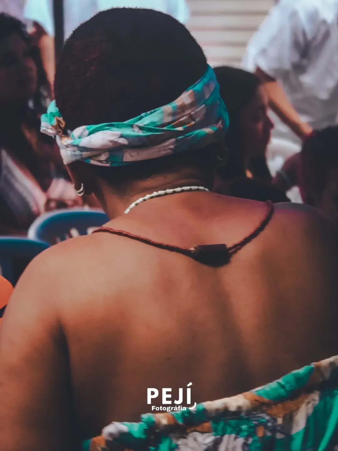 Pessoa com lenço colorido na cabeça, vista de costas durante uma celebração.