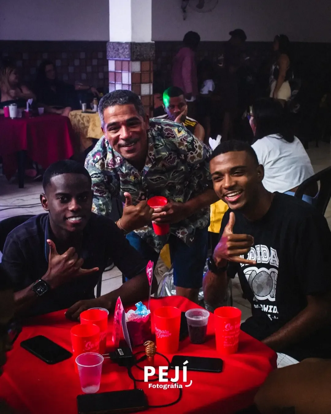 Três pessoas sorrindo, sentadas à mesa em uma festa de aniversário.