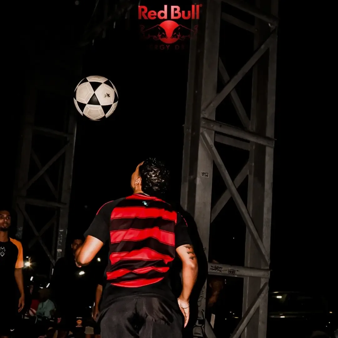 Homem de camisa listrada equilibrando uma bola em um espaço de evento à noite.