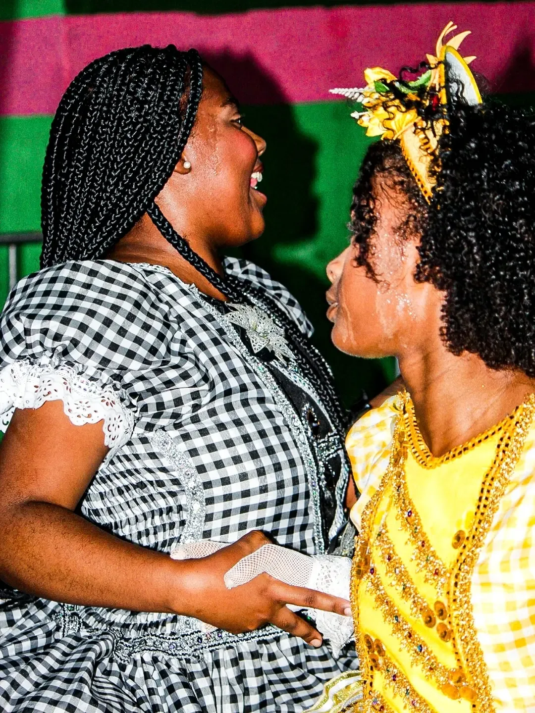 Duas mulheres conversando de perto, com roupas estampadas, em uma festa junina.
